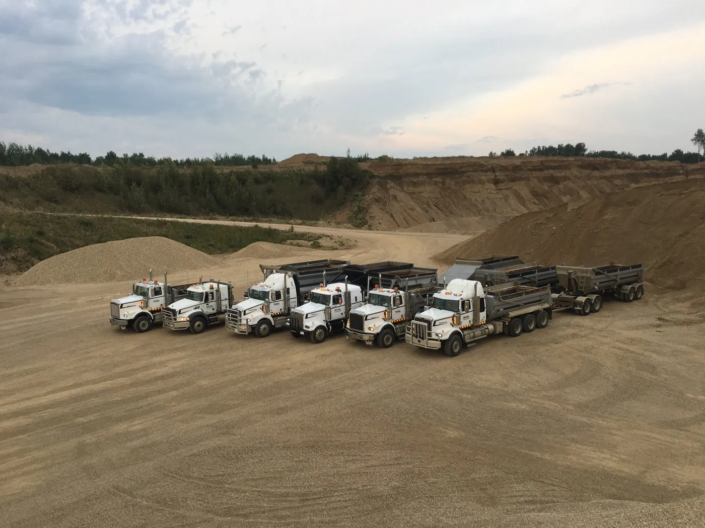 Row of Ruel Concrete tandem and end-dump gravel trucks staged in the pit